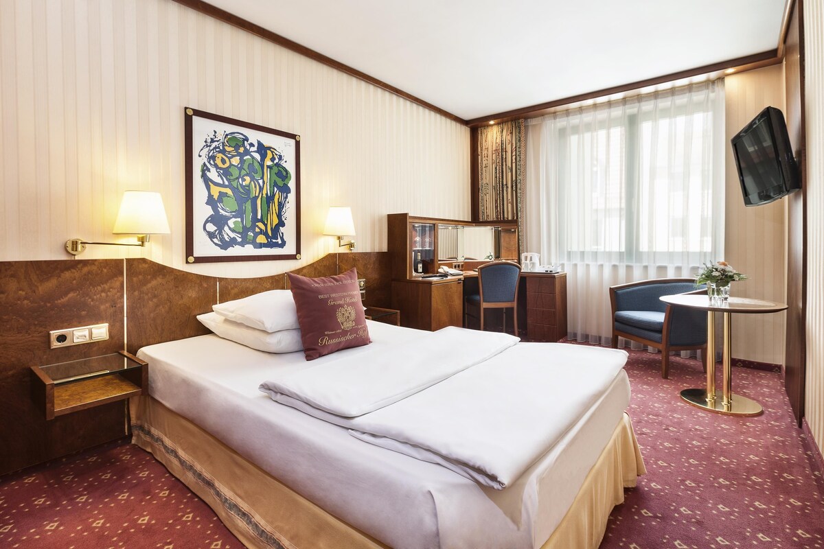 Une chambre d’hôtel avec un grand lit, des lampes de chevet, un bureau, une chaise, une télévision et une fenêtre avec des rideaux.
