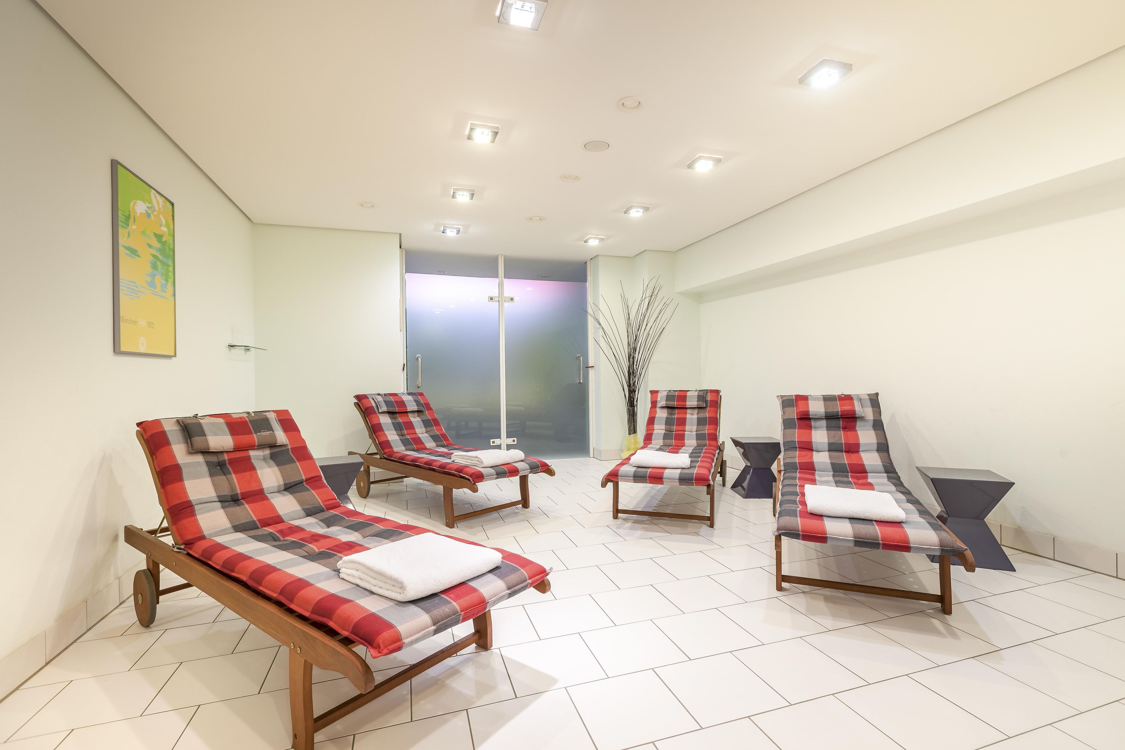 Een kamer met vier lounge fauteuils, een grote spiegel en een deur naar een andere ruimte.