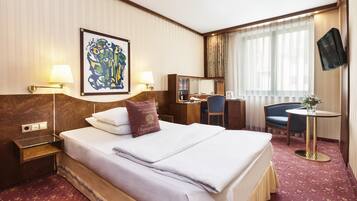 A hotel room with a large bed, bedside lamps, a desk, a chair, a television, and a window with curtains.