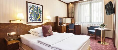 A hotel room with a large bed, bedside lamps, a desk, a chair, a television, and a window with curtains.