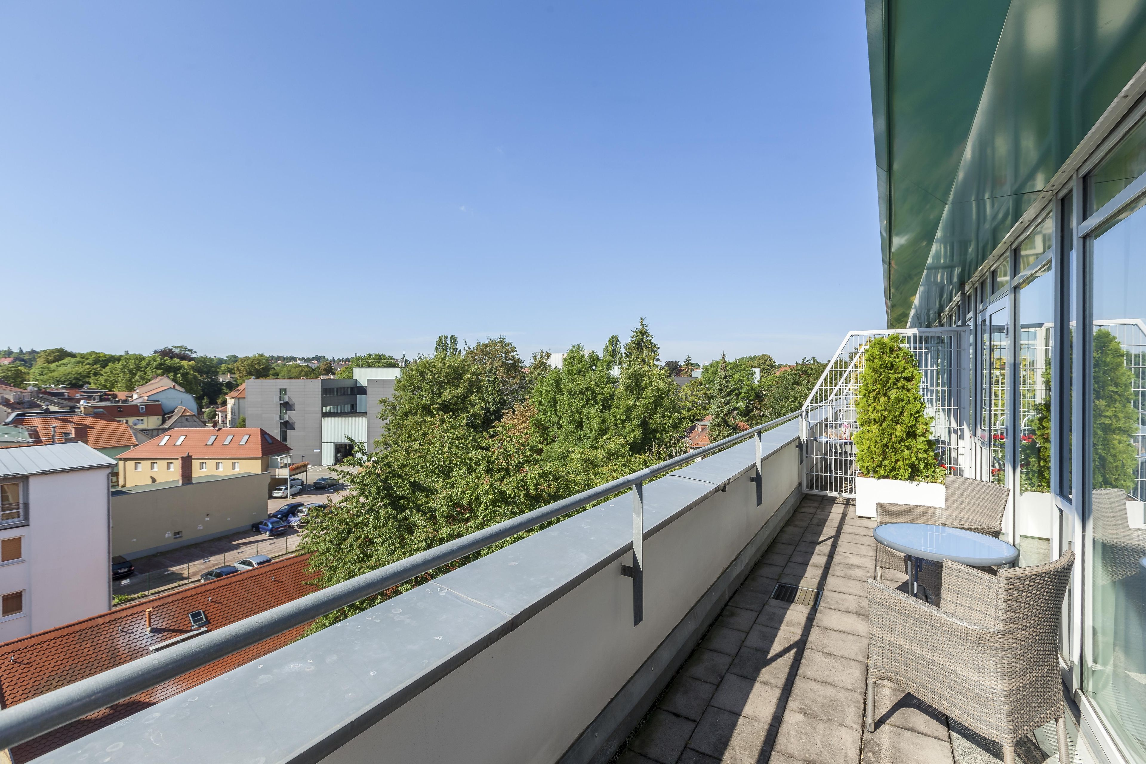 A balcony with a view of a cityscape, including buildings and trees.