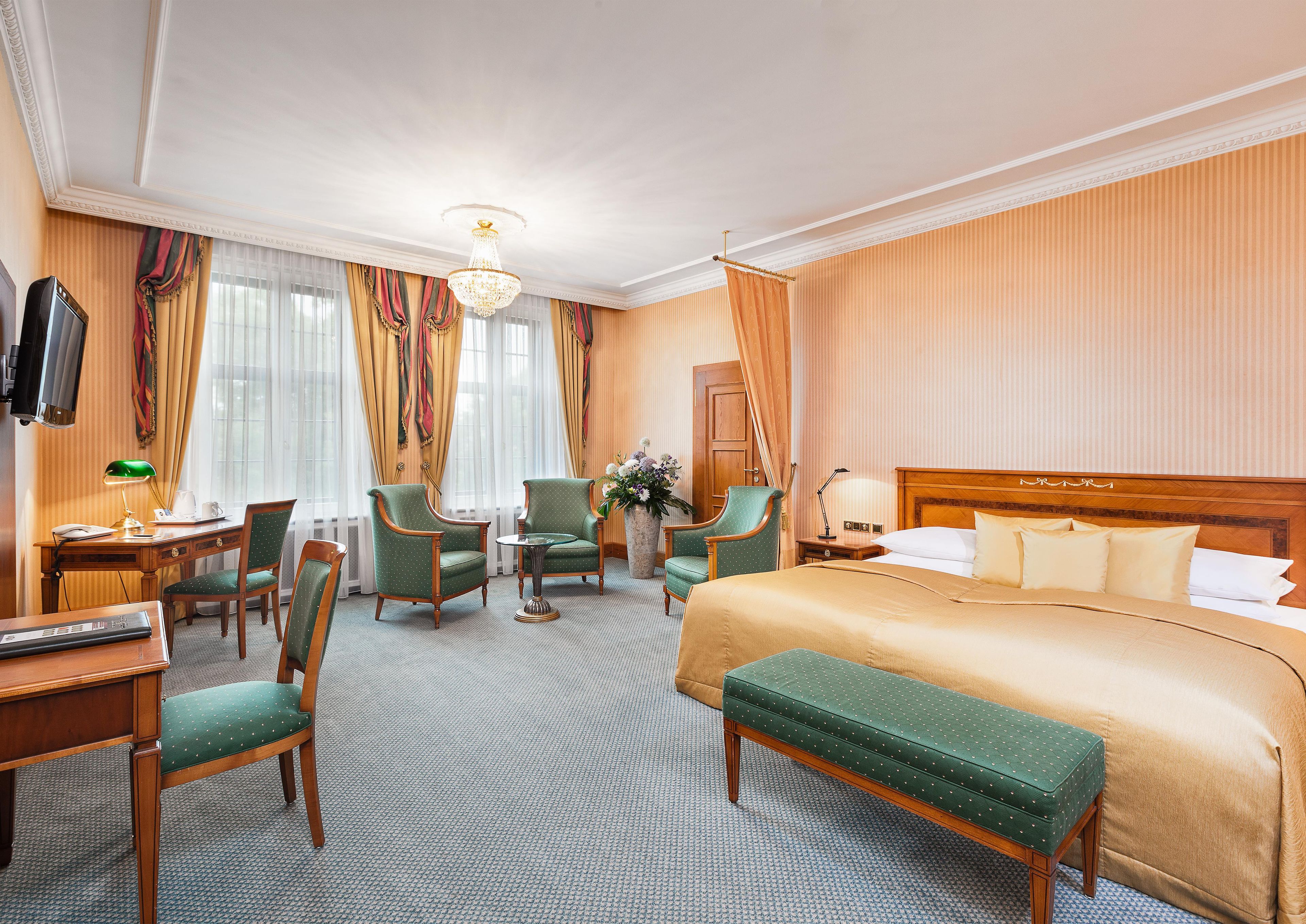 Ein Hotelzimmer mit einem großen Bett, zwei Sesseln, einem Schreibtisch mit Lampe und einem Fernseher.