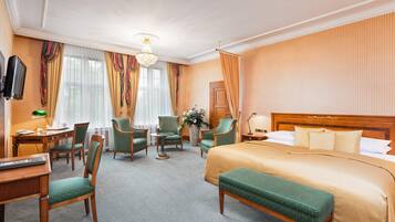 Ein Hotelzimmer mit einem großen Bett, zwei Sesseln, einem Schreibtisch mit Lampe und einem Fernseher.