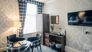 Habitación de hotel con ventana con cortinas a cuadros, un escritorio con espejo, televisión y una pequeña mesa con sillas.