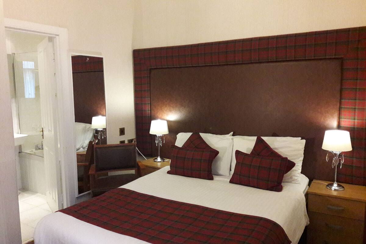 A hotel room with a large bed, two bedside tables, a mirror, and a red plaid headboard.