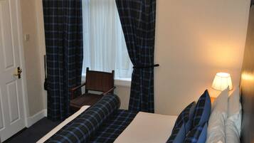A hotel room with a large bed, a bedside table with a lamp, a chair, and a window with curtains.