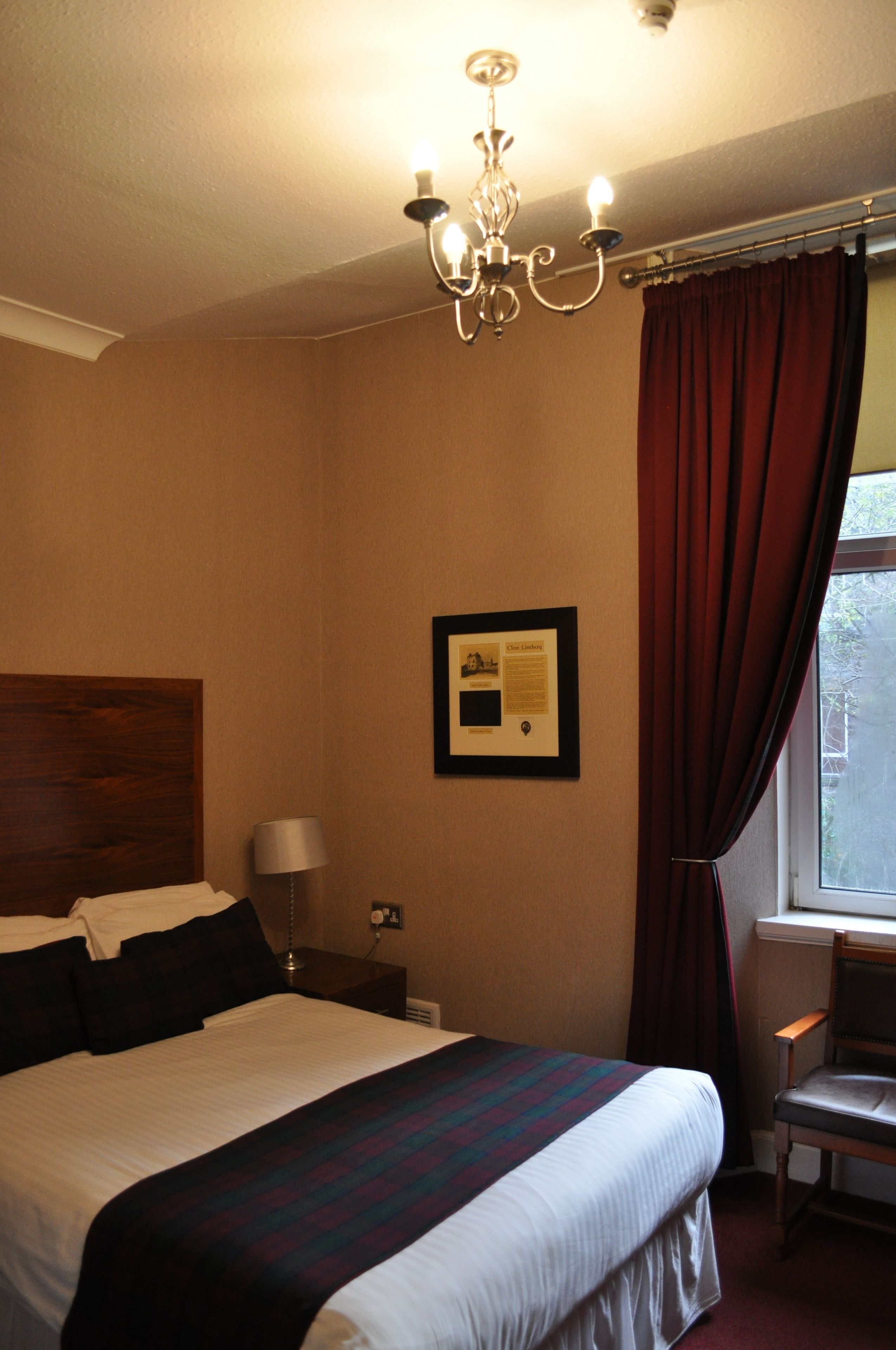 Une chambre d’hôtel avec un grand lit, un lustre, un certificat encadré accroché au mur et une fenêtre avec des rideaux.