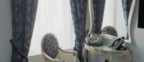 Een hotelkamer met een bed, een stoel, een kaptafel met spiegel, een telefoon en een raam met gordijnen.