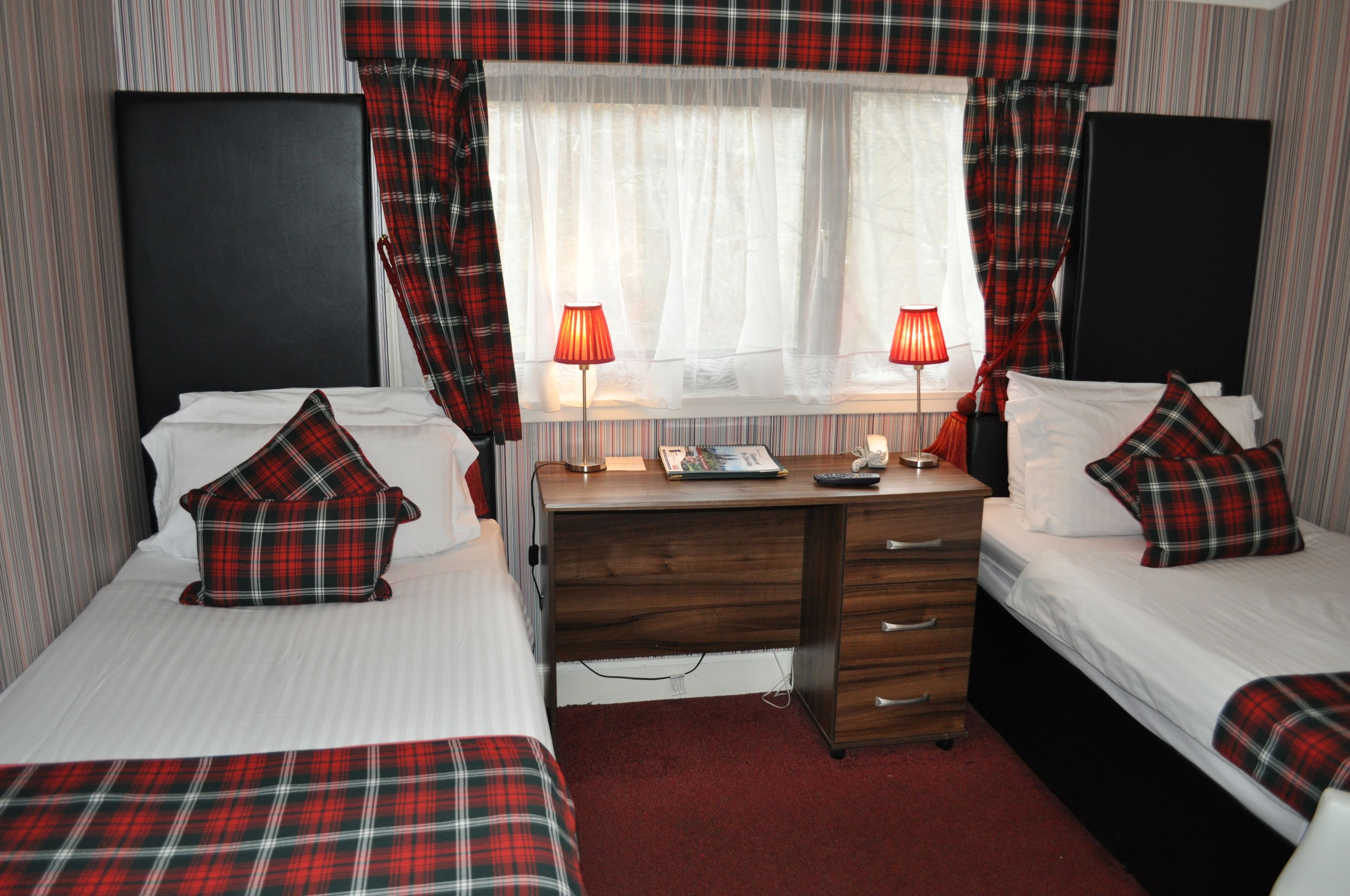 A hotel room with two beds, a desk, and a window with curtains.