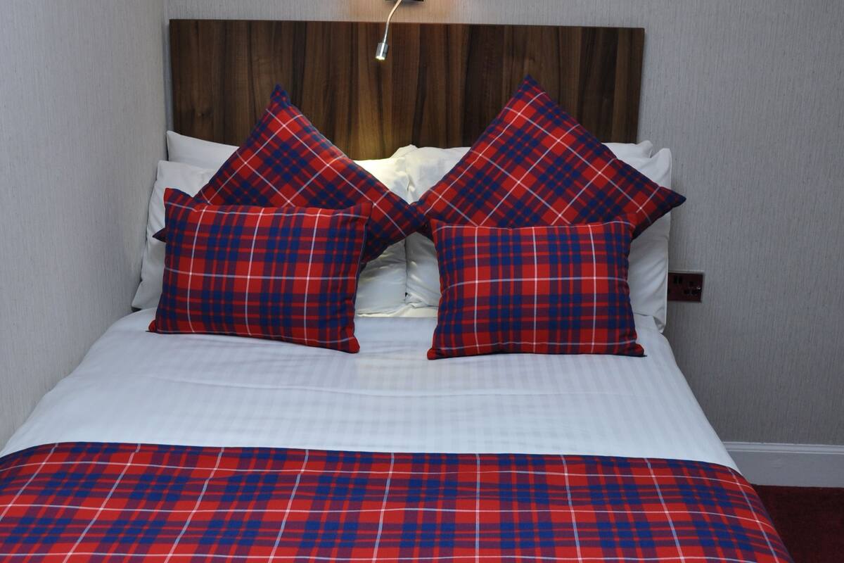 A bed with a red and blue plaid bedspread, two matching pillows, and a wooden headboard.