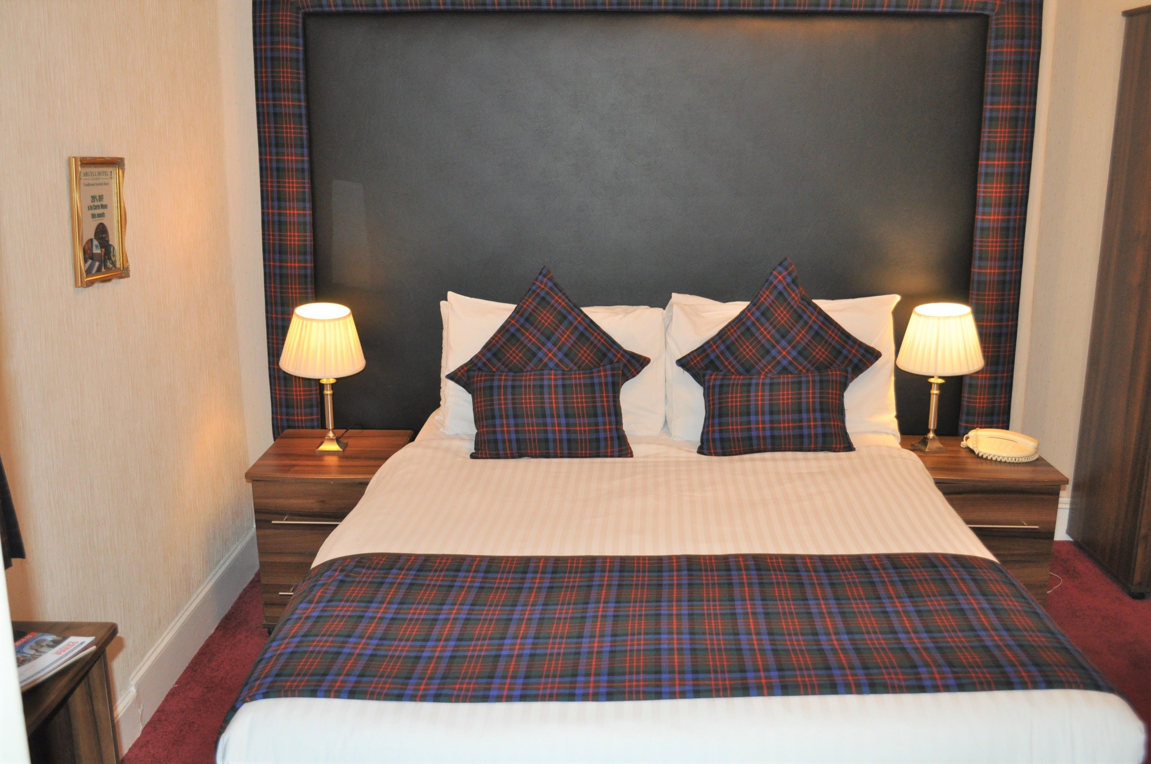 A neatly made bed with plaid bedding, two bedside lamps, and a framed picture on the wall.