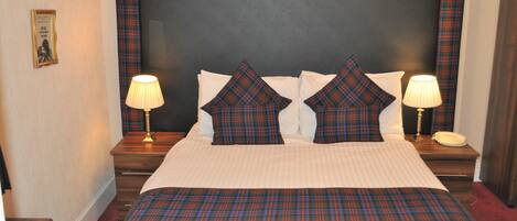 A neatly made bed with plaid bedding, two bedside lamps, and a framed picture on the wall.