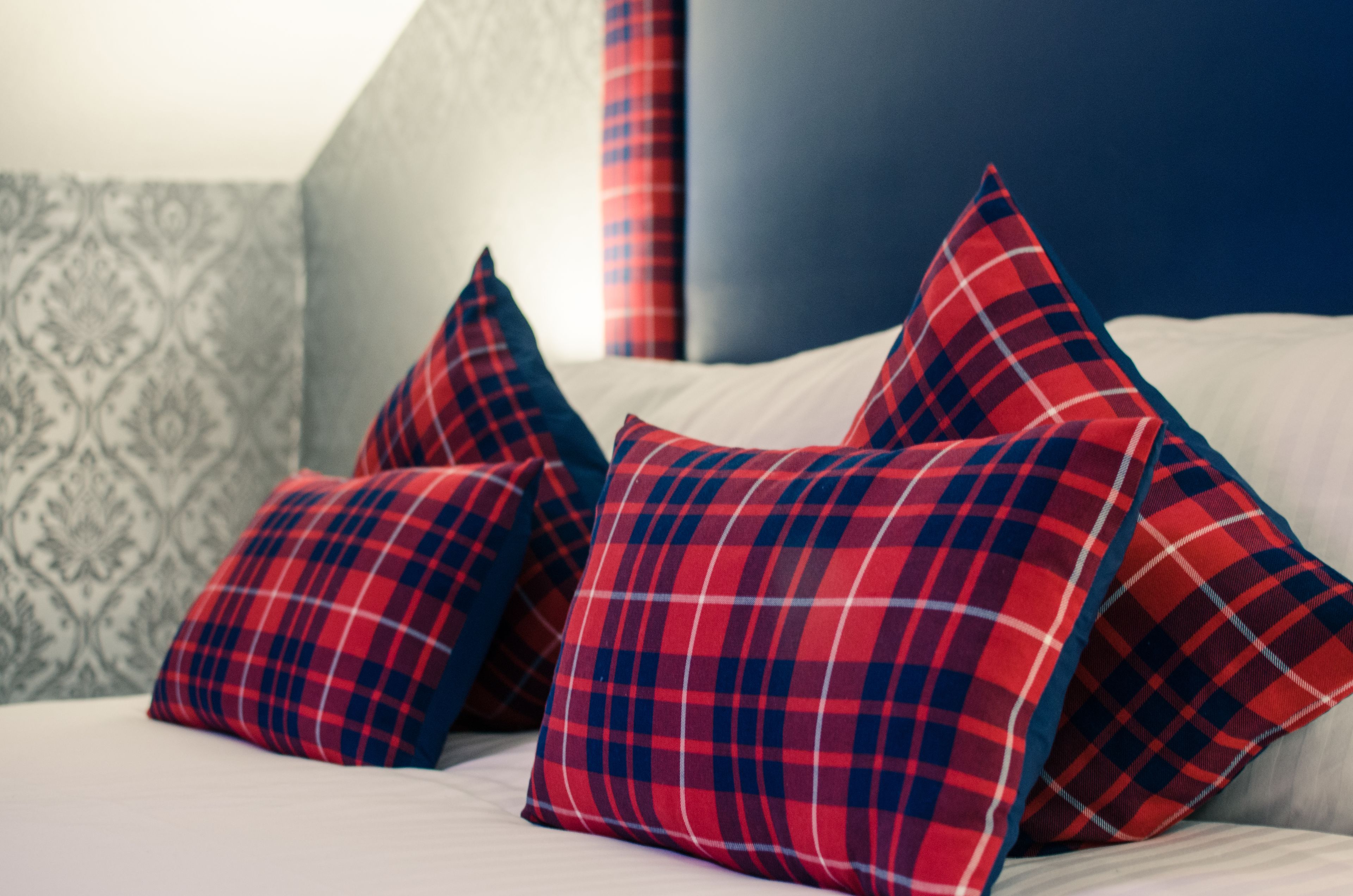 A bed with red and blue plaid pillows and a patterned wall.