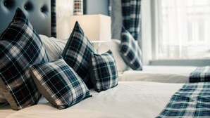 Una cama con ropa de cama y almohadas a cuadros, un cabecero capitonado y una ventana con cortinas.