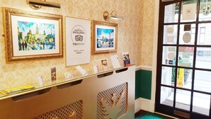 Un área de recepción con obras de arte enmarcadas, un certificado de TripAdvisor y una vitrina de vidrio con folletos.
