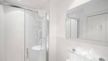 A modern bathroom with a glass shower enclosure, a large mirror, and a glass shelf with toiletries.