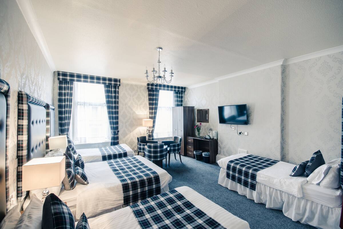 A hotel room with two beds, a desk, a chair, a TV, and a chandelier.