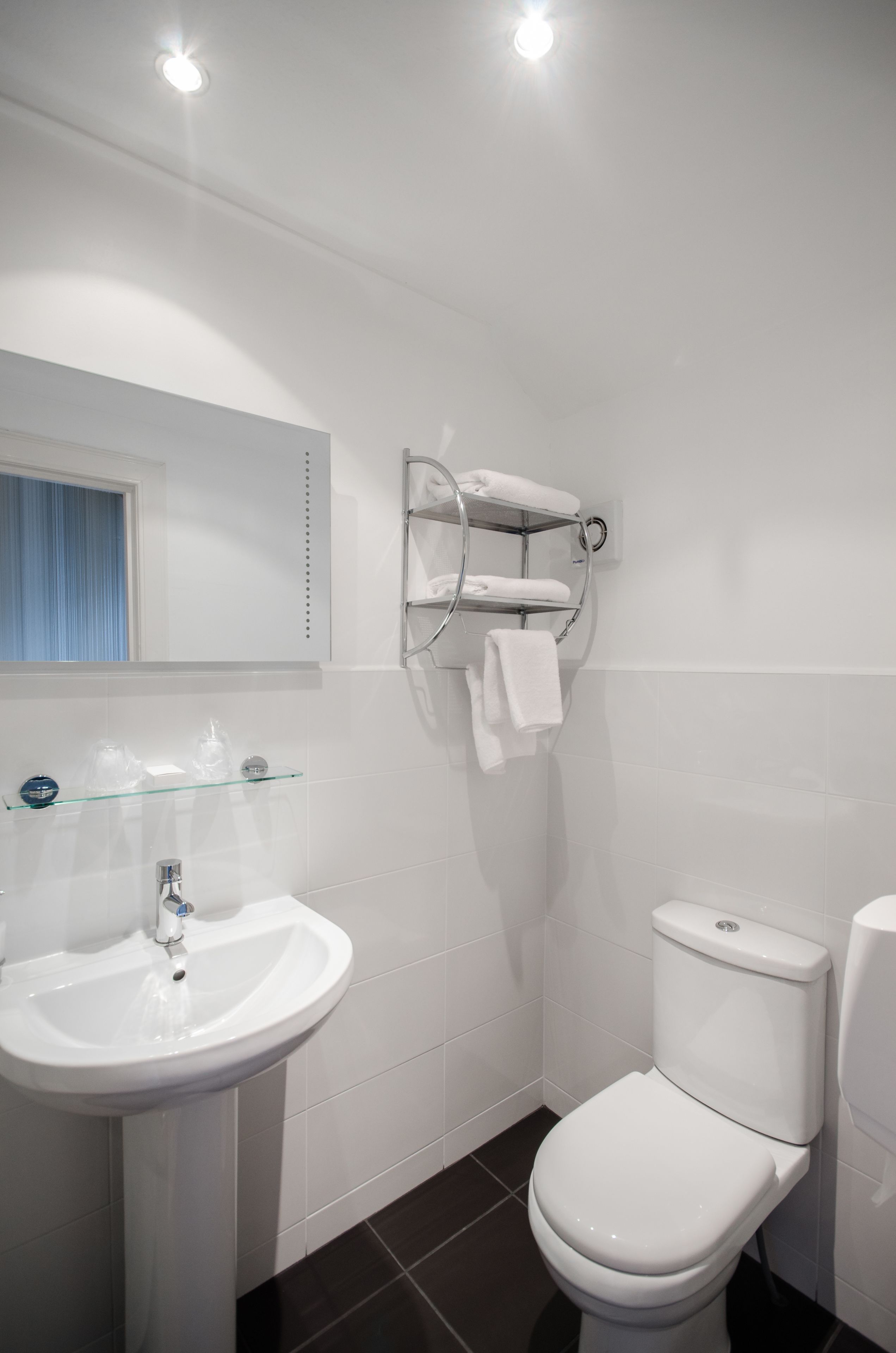 A modern bathroom with a white sink, a toilet, and a glass shelf with toiletries.
