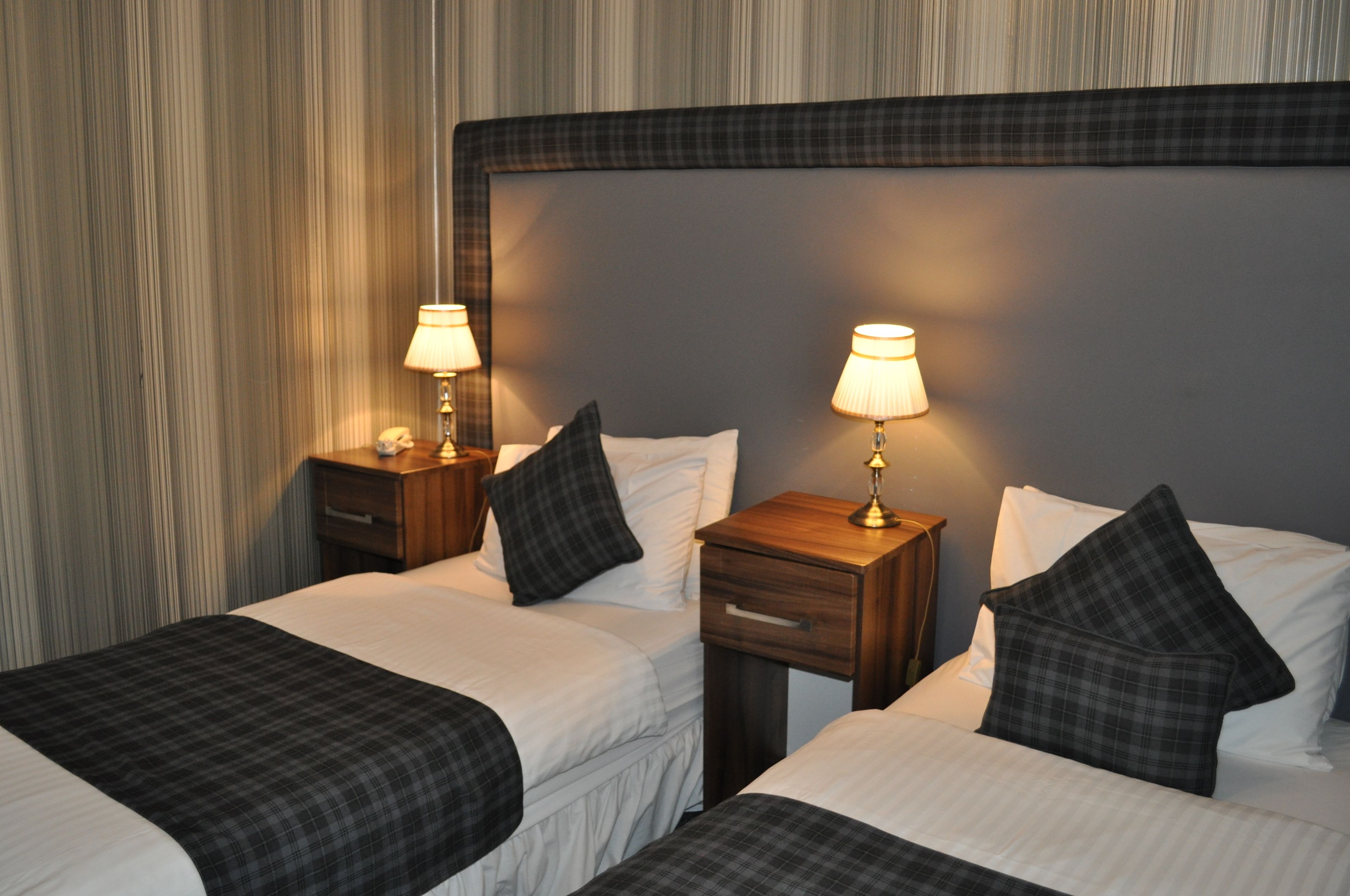 Habitación de hotel con dos camas, cada una con una mesita de noche, una lámpara y un teléfono.