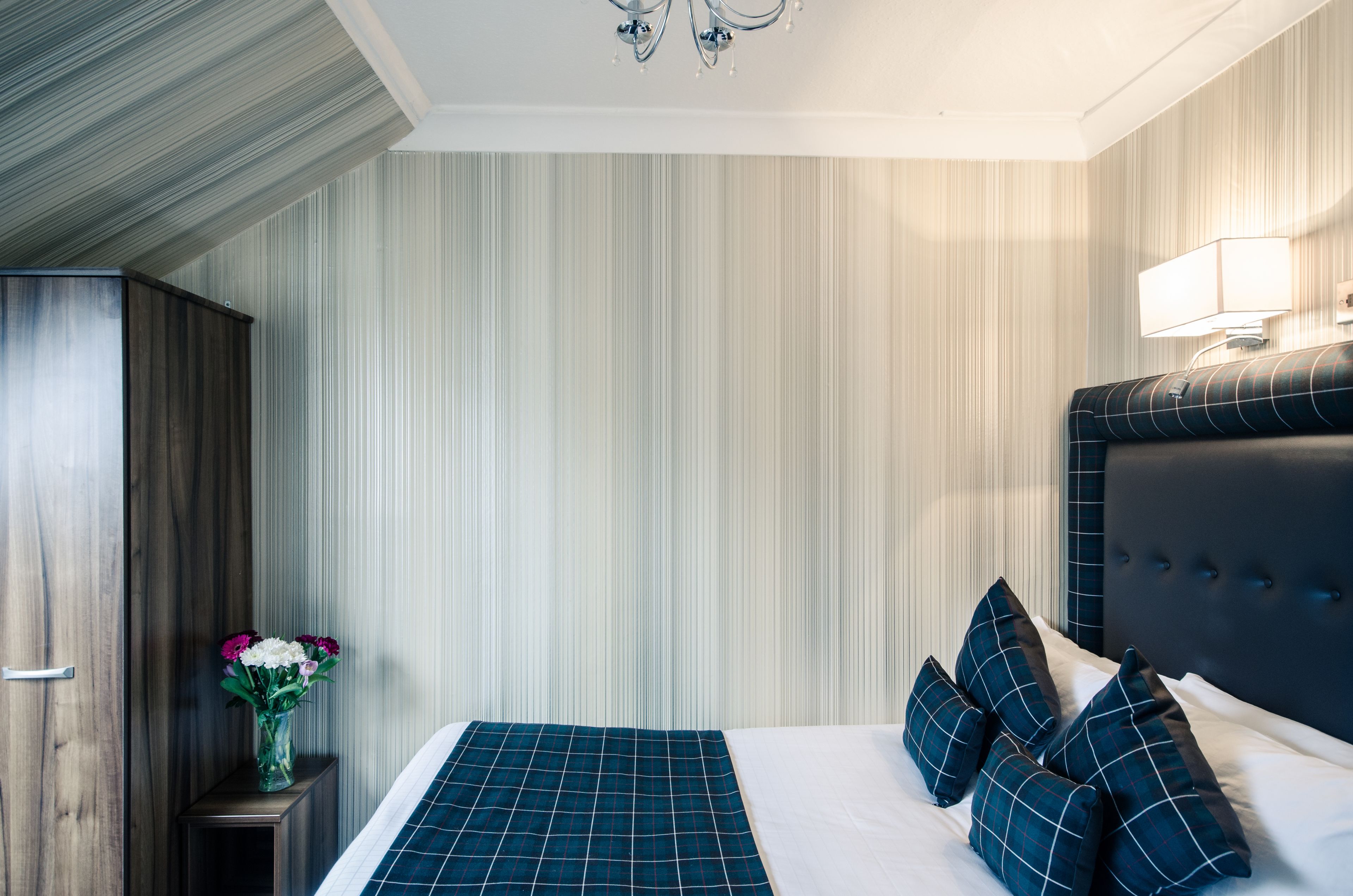 Une chambre d’hôtel avec un lit, une table de chevet, un vase de fleurs, un lustre et une tête de lit.