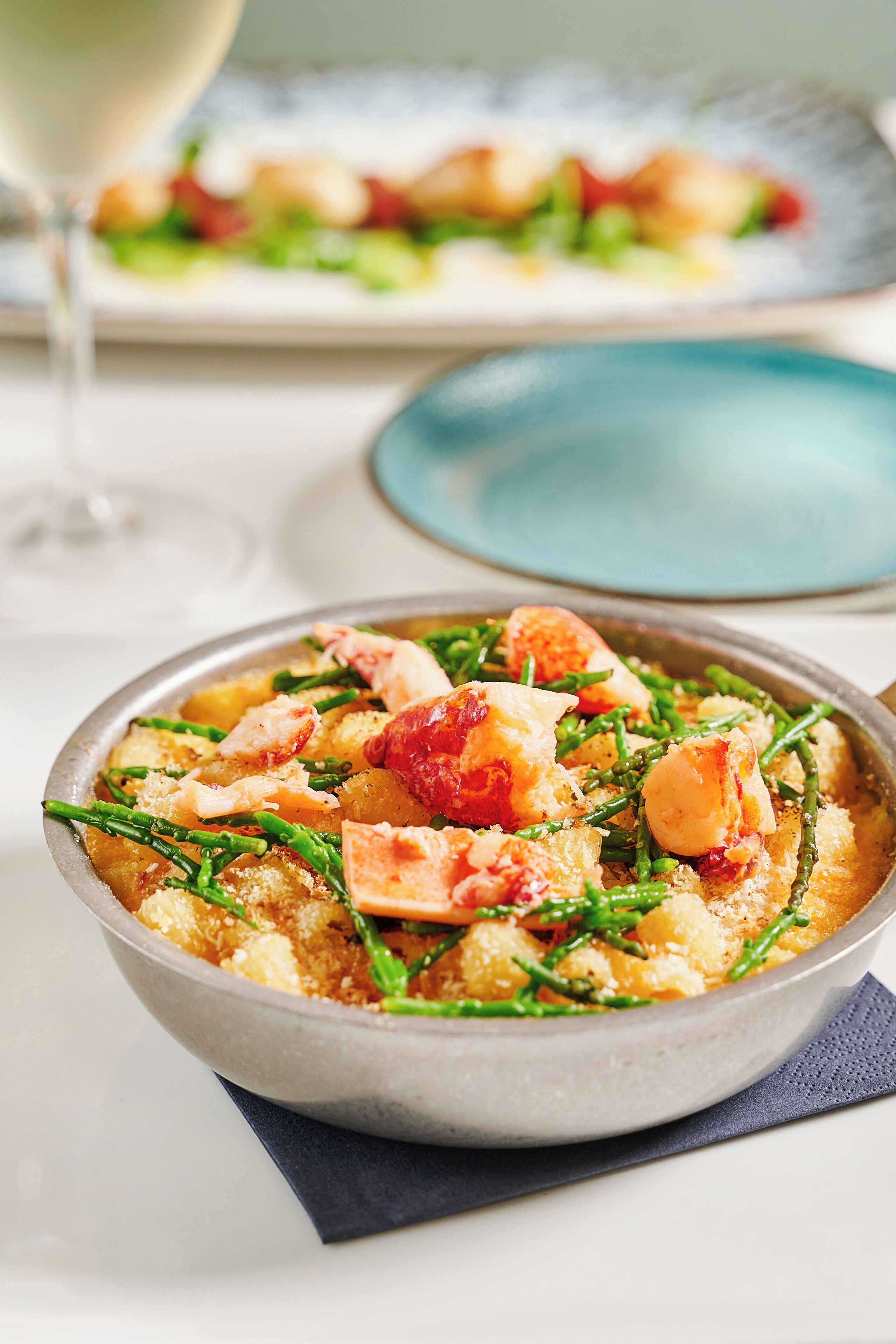A bowl of seafood pasta with green beans and shrimp, served on a metal plate with a blue napkin underneath.
