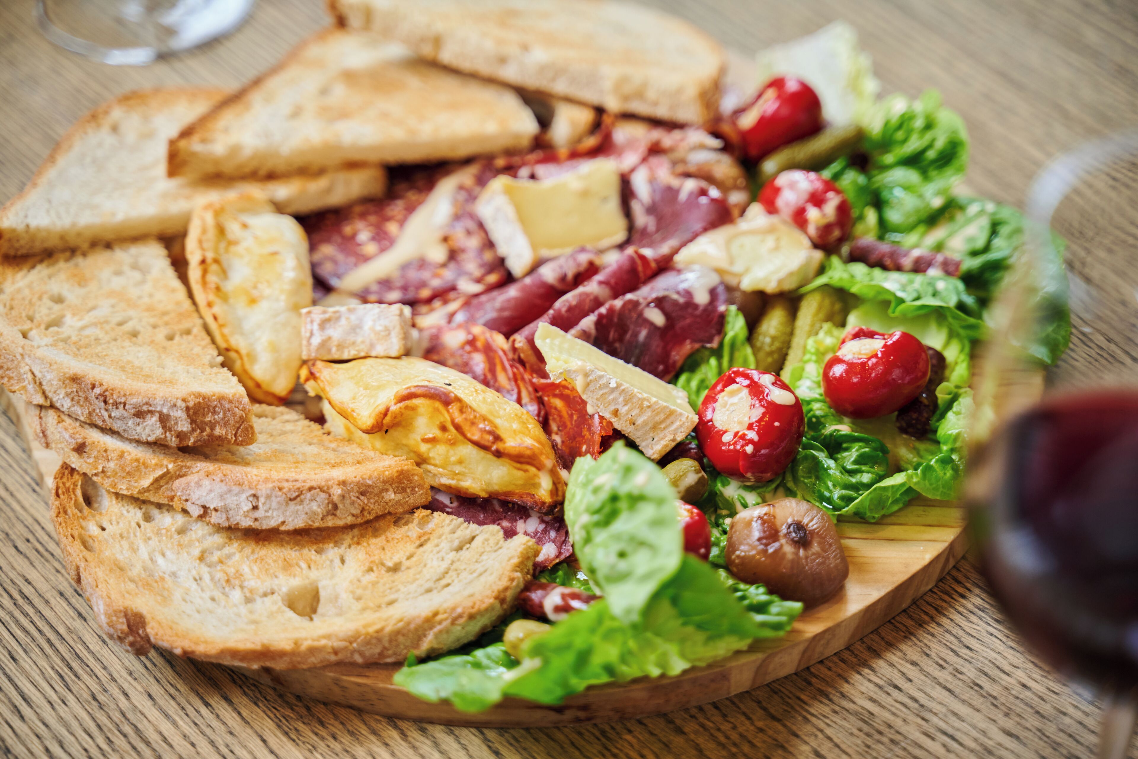 A wooden board with various food items including bread, cheese, and vegetables.