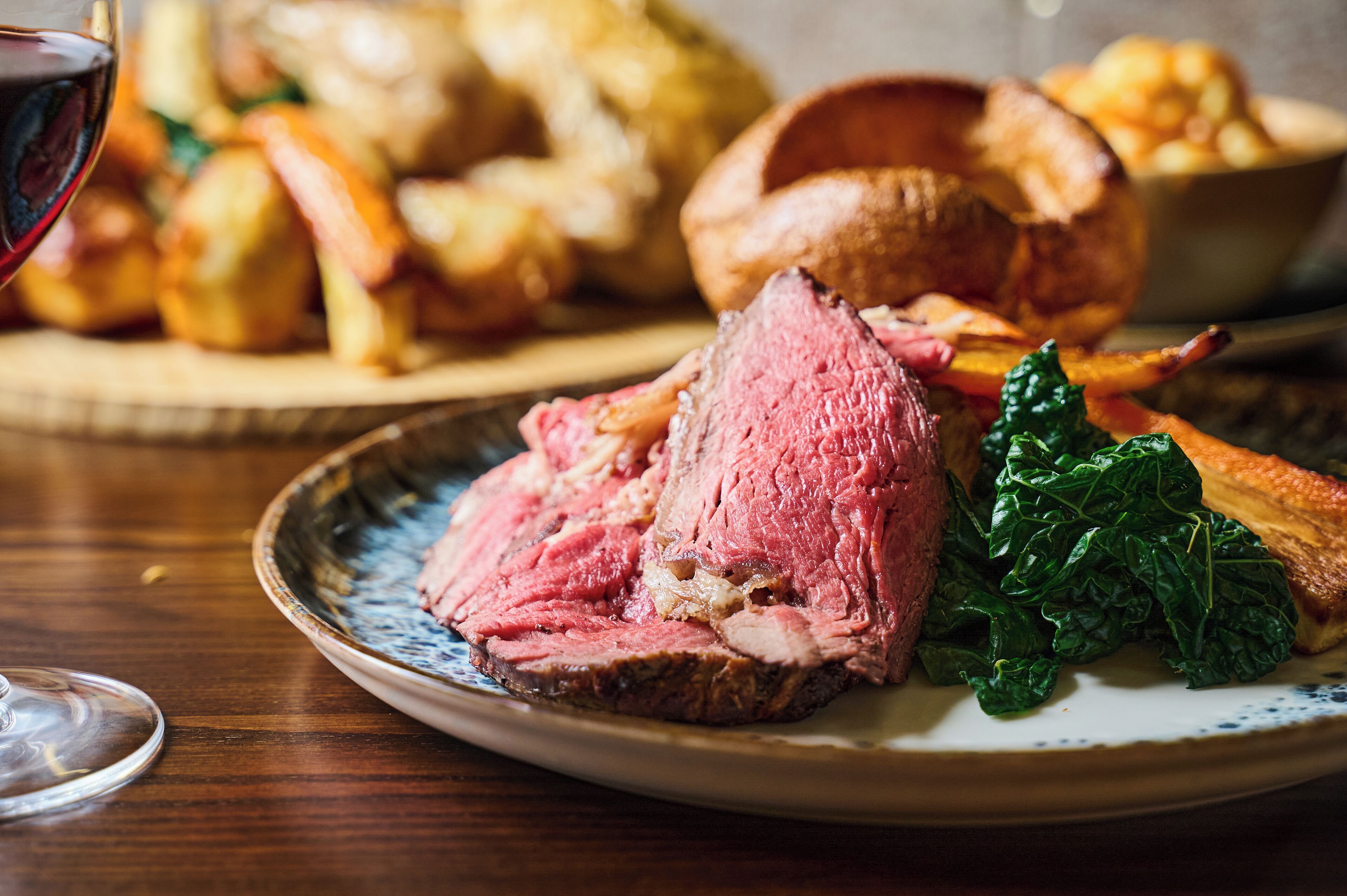 A plate of sliced roast beef with vegetables and a glass of red wine.
