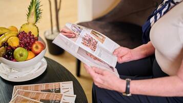 Una persona leyendo una revista con un frutero sobre una mesa.