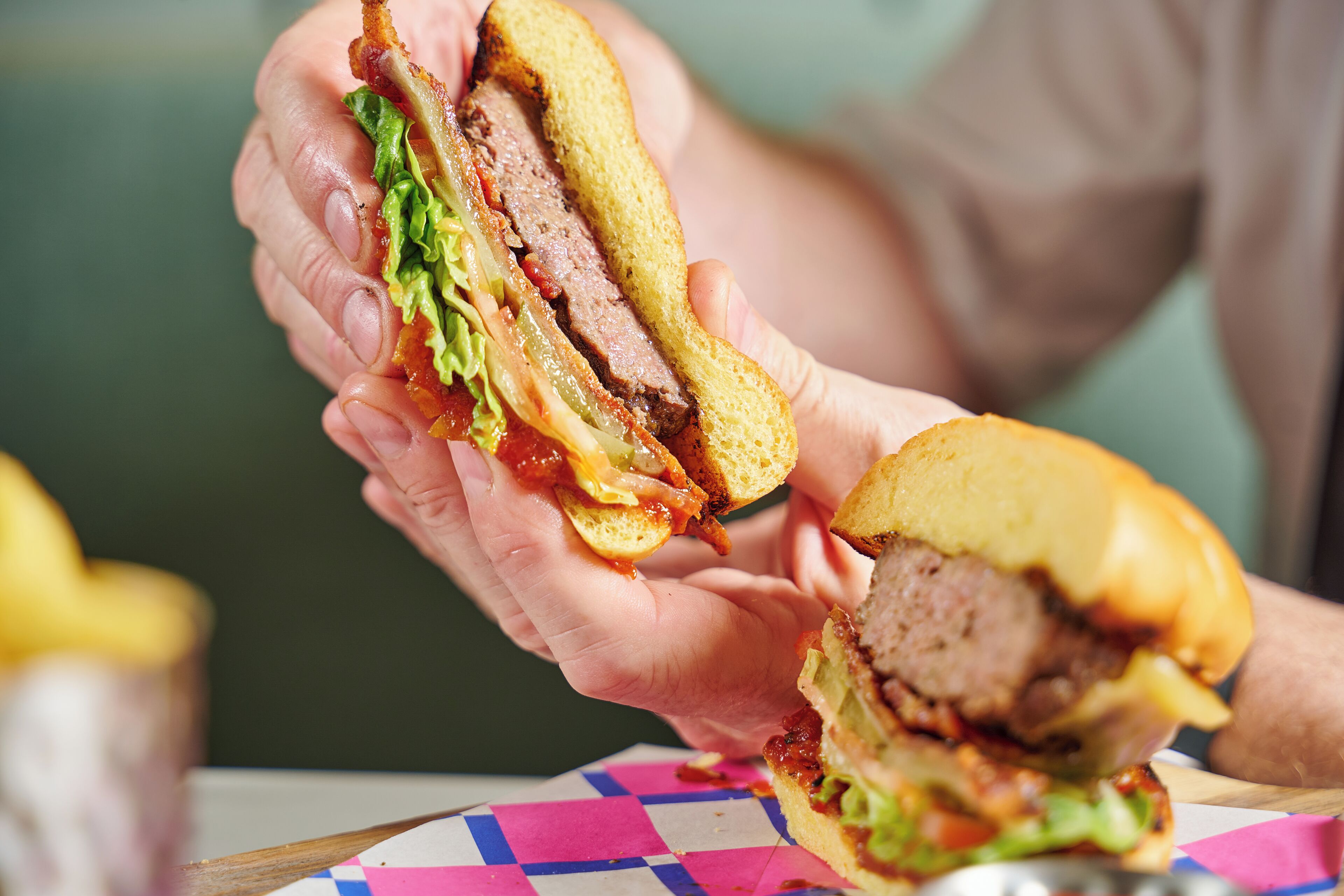 A person holding a sandwich with visible layers of meat, lettuce, and cheese.