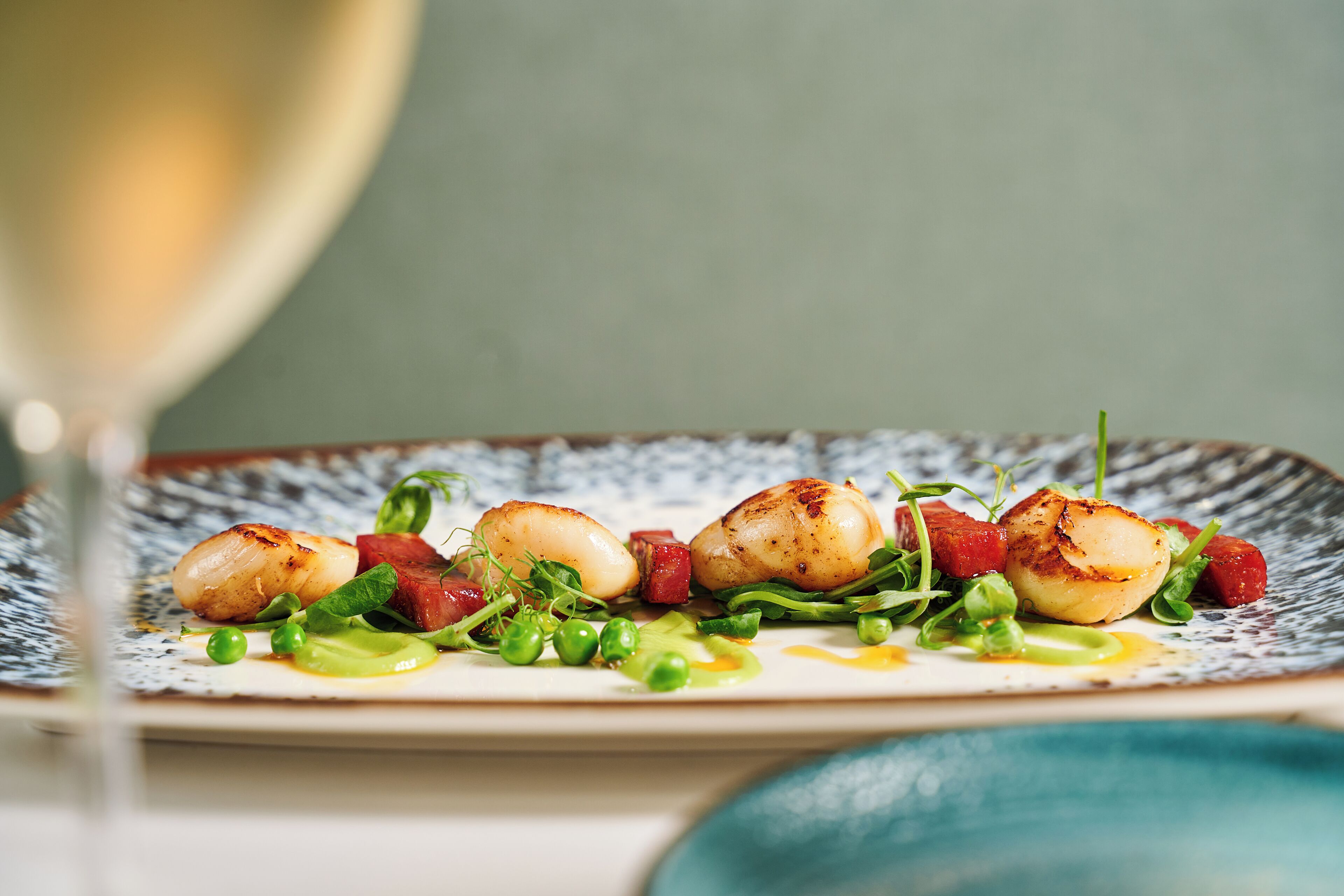 A plate of food with seared scallops, greens, and a sauce.