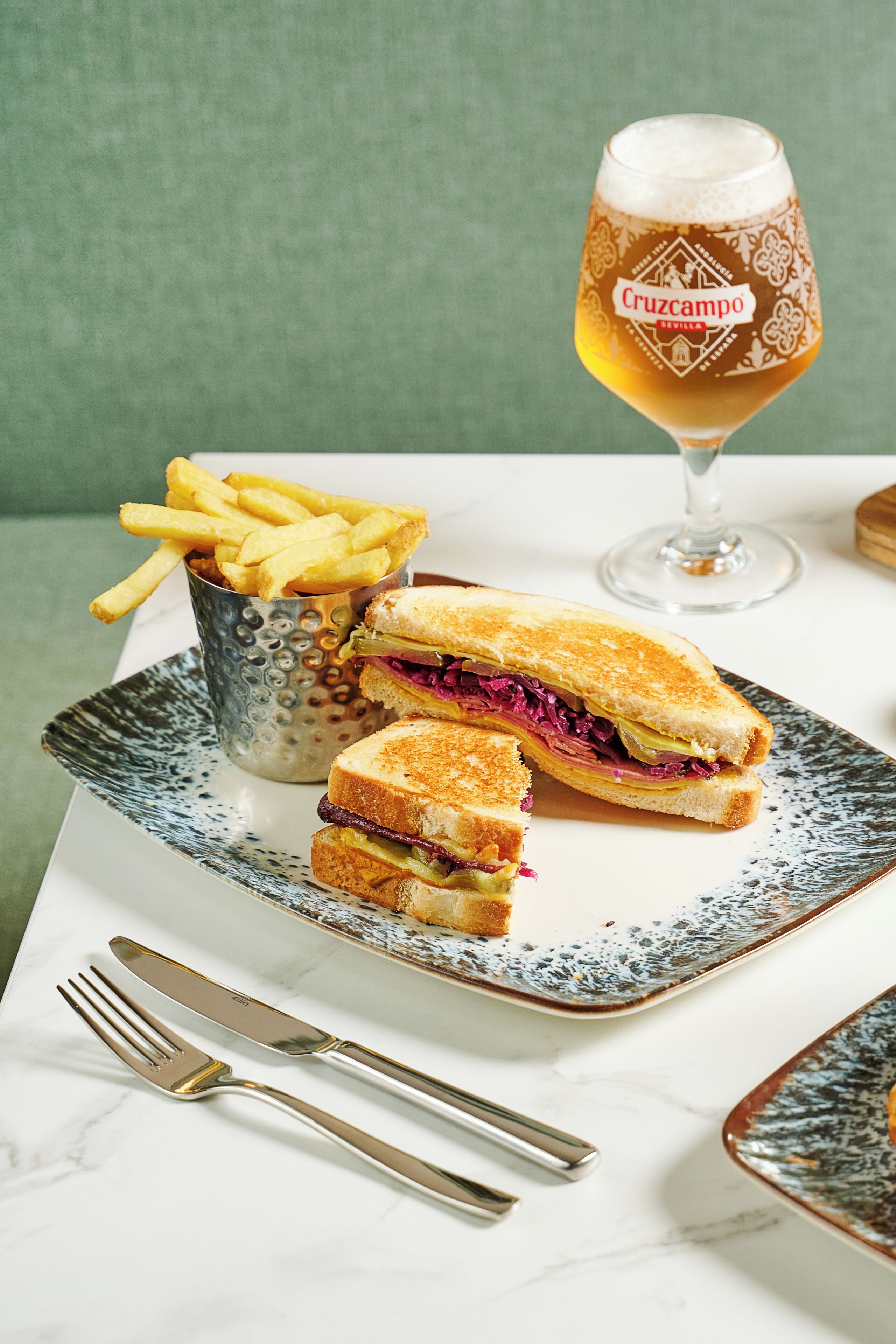 A sandwich cut in half, a glass of beer, and a container of fries on a table.