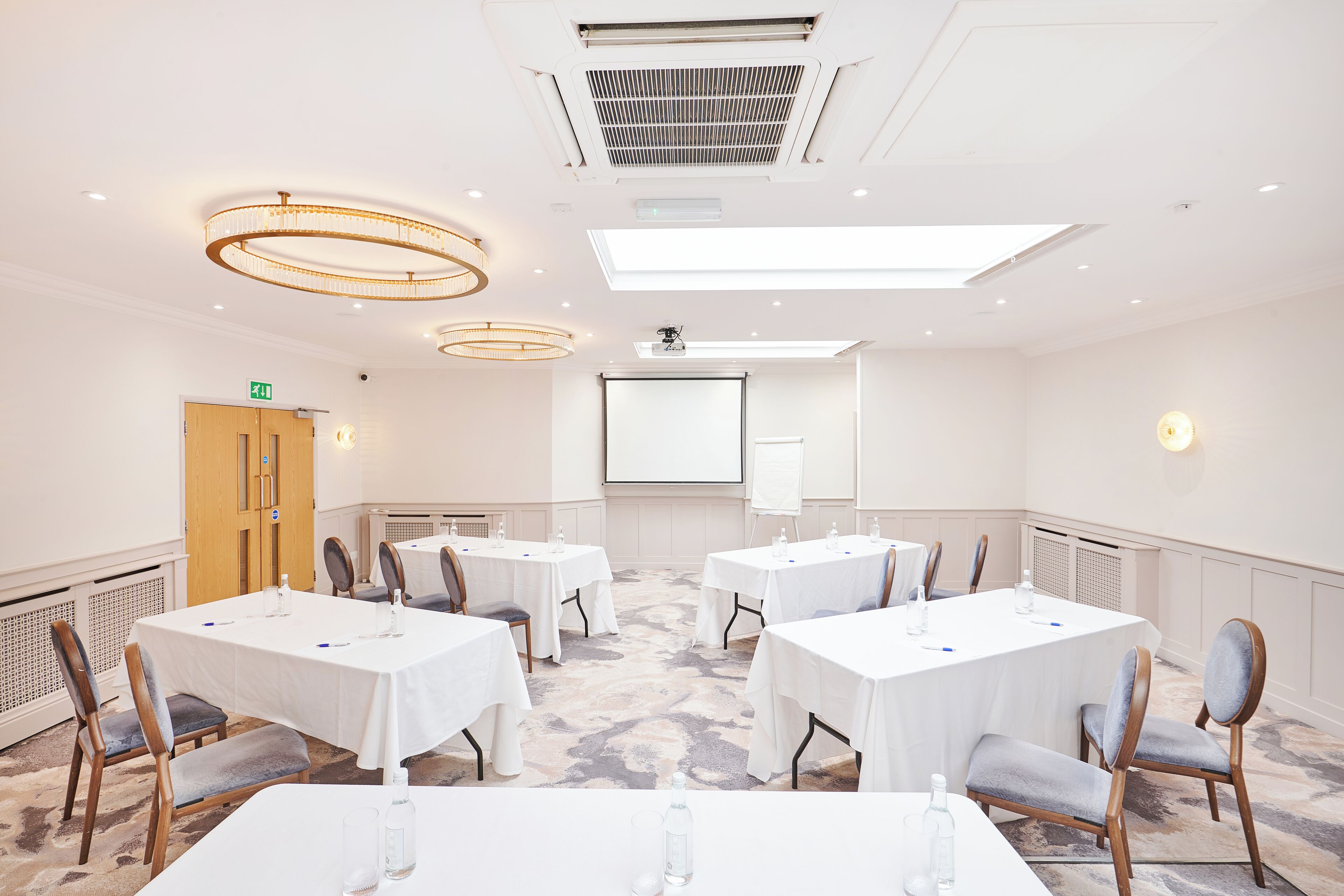 A conference room with white tables, chairs, a projector screen, and a whiteboard.