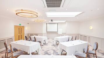 A conference room with white tables, chairs, a projector screen, and a whiteboard.