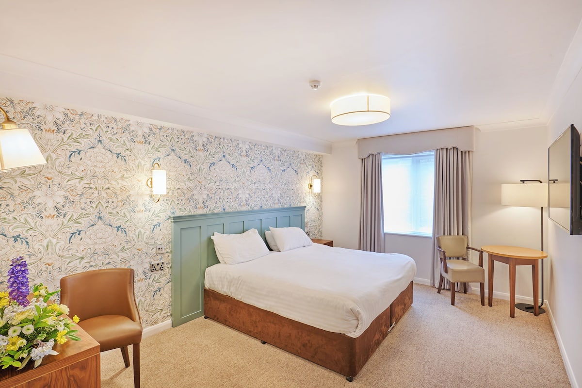 Ein Hotelzimmer mit Bett, Sessel, Tisch und Schreibtisch.