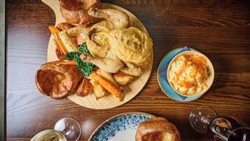 Een houten tafel met een gebraden kip, Yorkshire pudding, geroosterde aardappelen en een schaal met gepureerde aardappelen.
