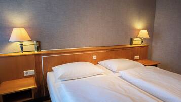 Habitación de hotel con dos camas individuales, cabeceros de madera, mesitas de noche y lámparas.