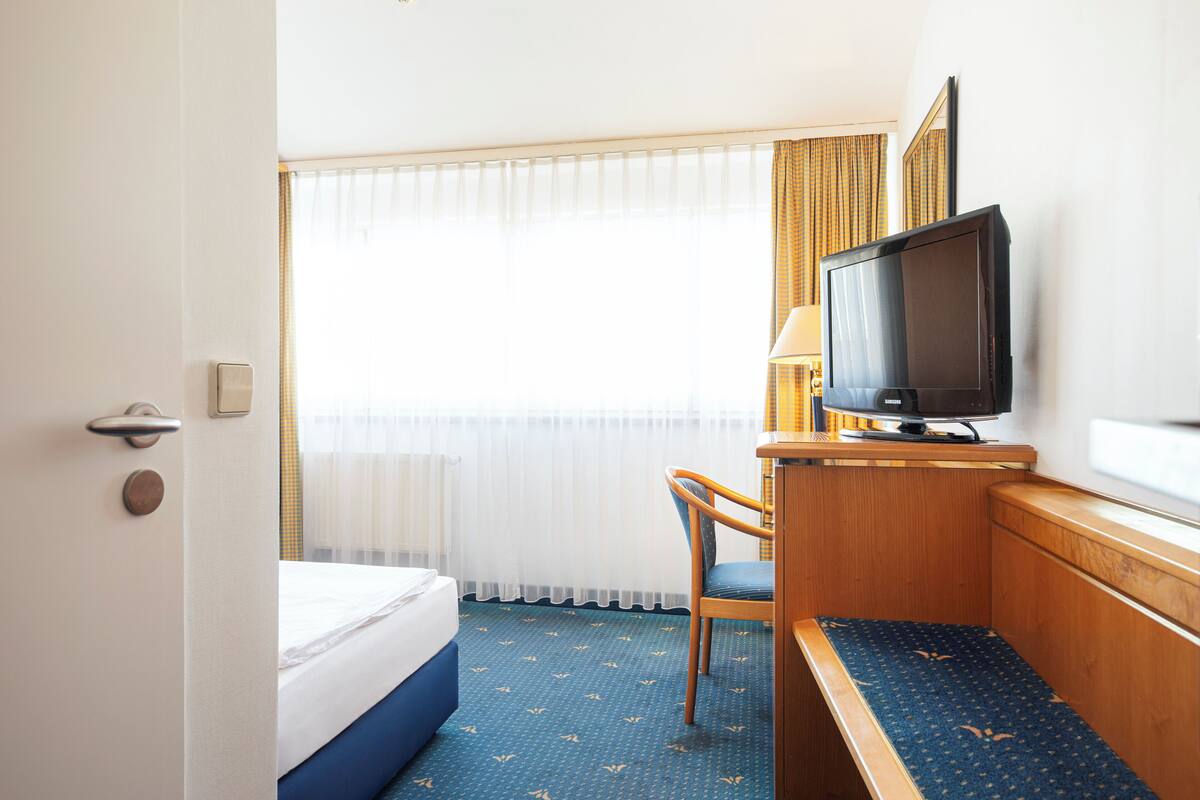 A hotel room with a bed, a desk with a television, a chair, and a window with curtains.