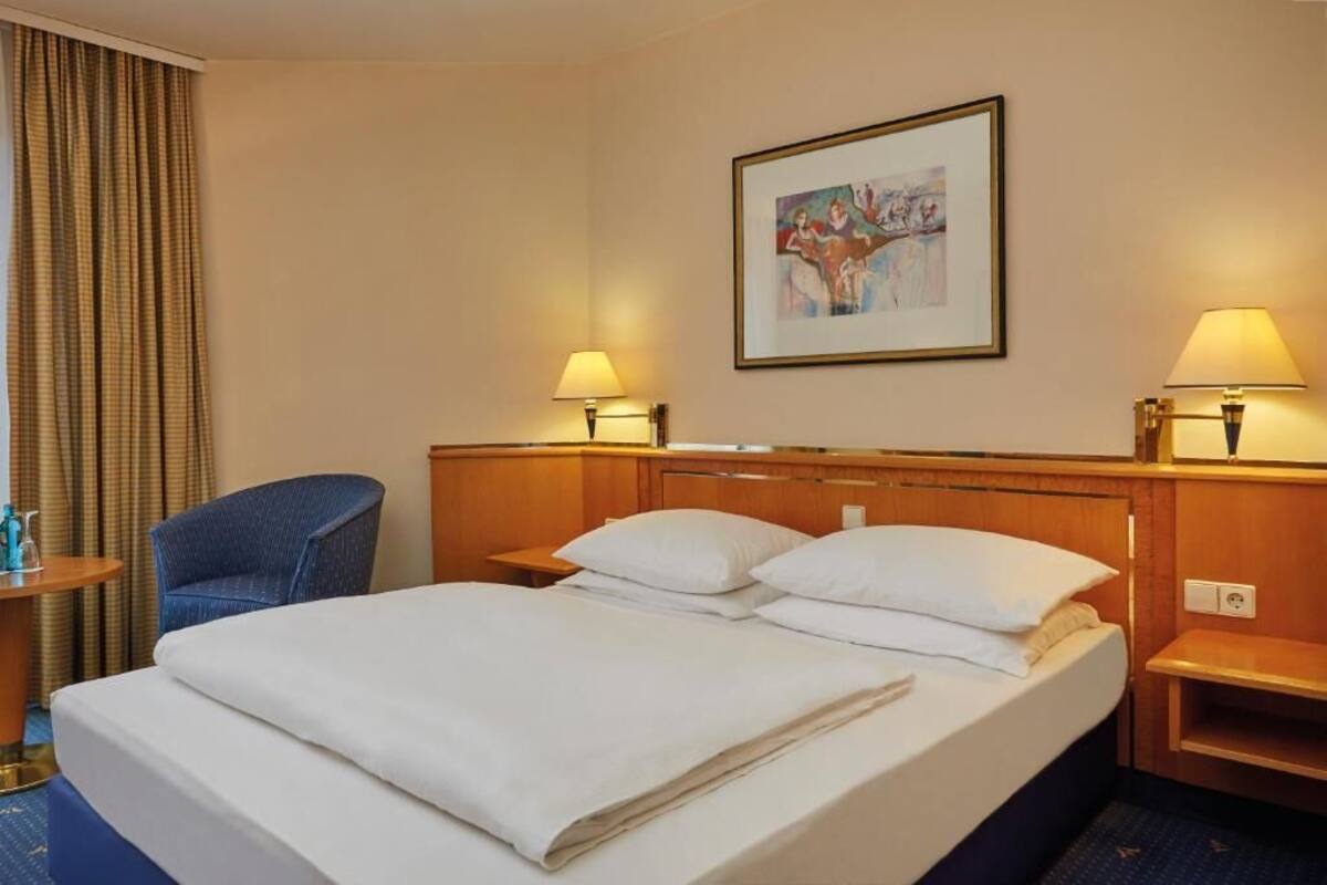 A hotel room with a large bed, two bedside tables, a chair, and a painting on the wall.
