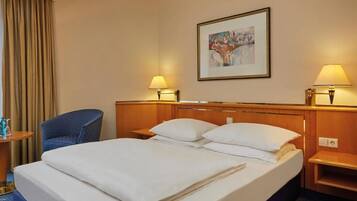 Habitación de hotel con una cama grande, dos mesitas de noche, una silla y un cuadro en la pared.