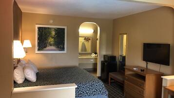 A hotel room with a bed, a desk, a dresser, a TV, a mirror, and a bathroom visible through an archway.