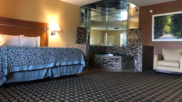 Ein Hotelzimmer mit Bett, Sitzecke, Badezimmer mit Glasabtrennung und einem großen Spiegel.