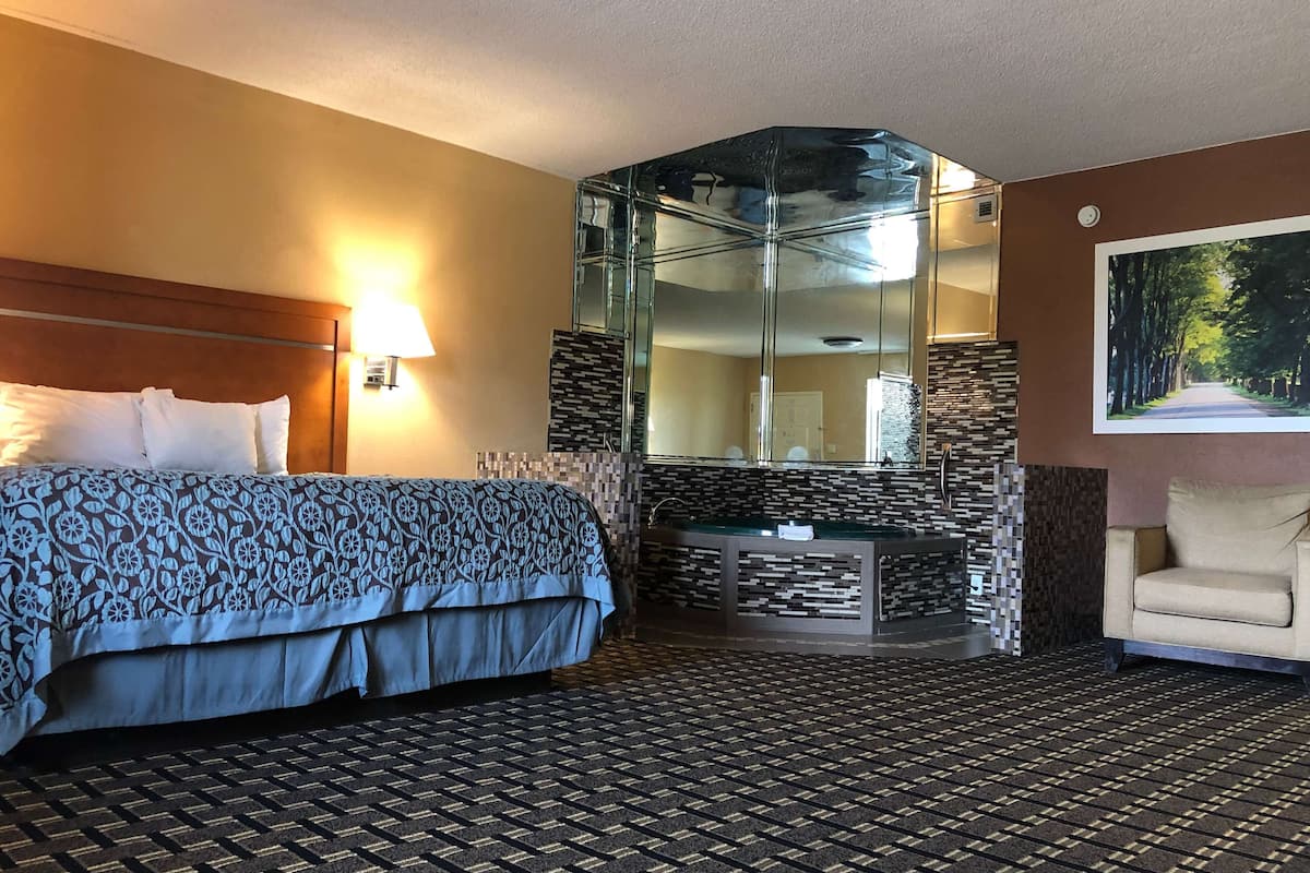A hotel room with a bed, a sitting area, a bathroom with a glass enclosure, and a large mirror.
