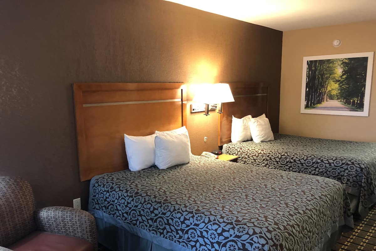 A hotel room with two beds, a headboard, a lamp, a telephone, and a painting on the wall.