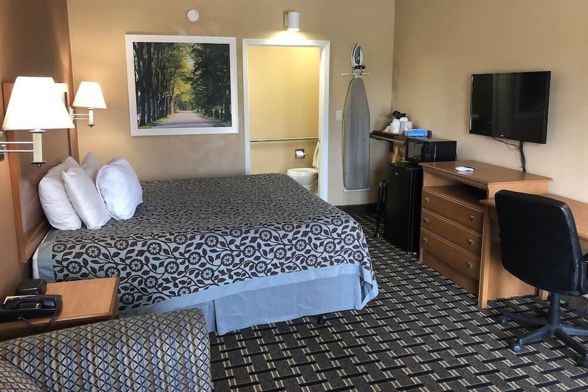 A hotel room with a bed, desk, chair, TV, and a painting on the wall.