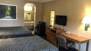 Une chambre d’hôtel avec deux lits, un bureau, une chaise, une télévision, un miroir, un réfrigérateur et une salle de bain visible à travers une arche.