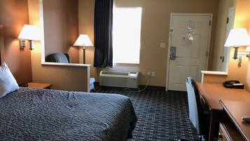 Habitación de hotel con una cama grande, dos lámparas de noche, una ventana con cortinas, un equipo de aire acondicionado, un escritorio con una silla y una puerta con cerradura.