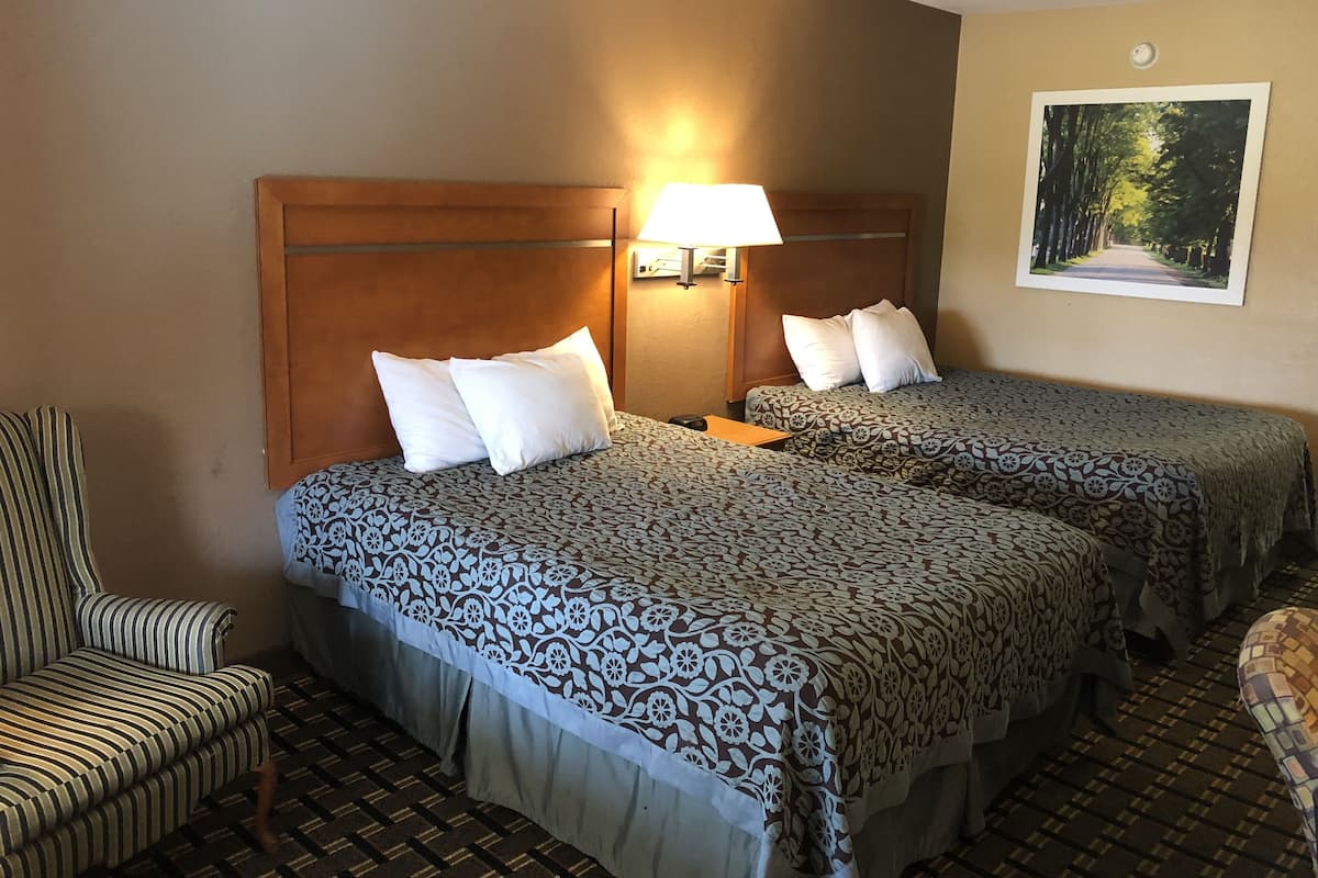 A hotel room with two beds, a chair, a lamp, and a framed picture on the wall.