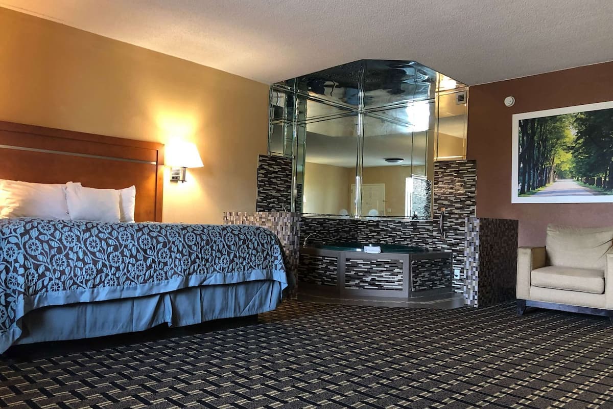 A hotel room with a bed, a bathroom vanity, a mirror, and a chair.