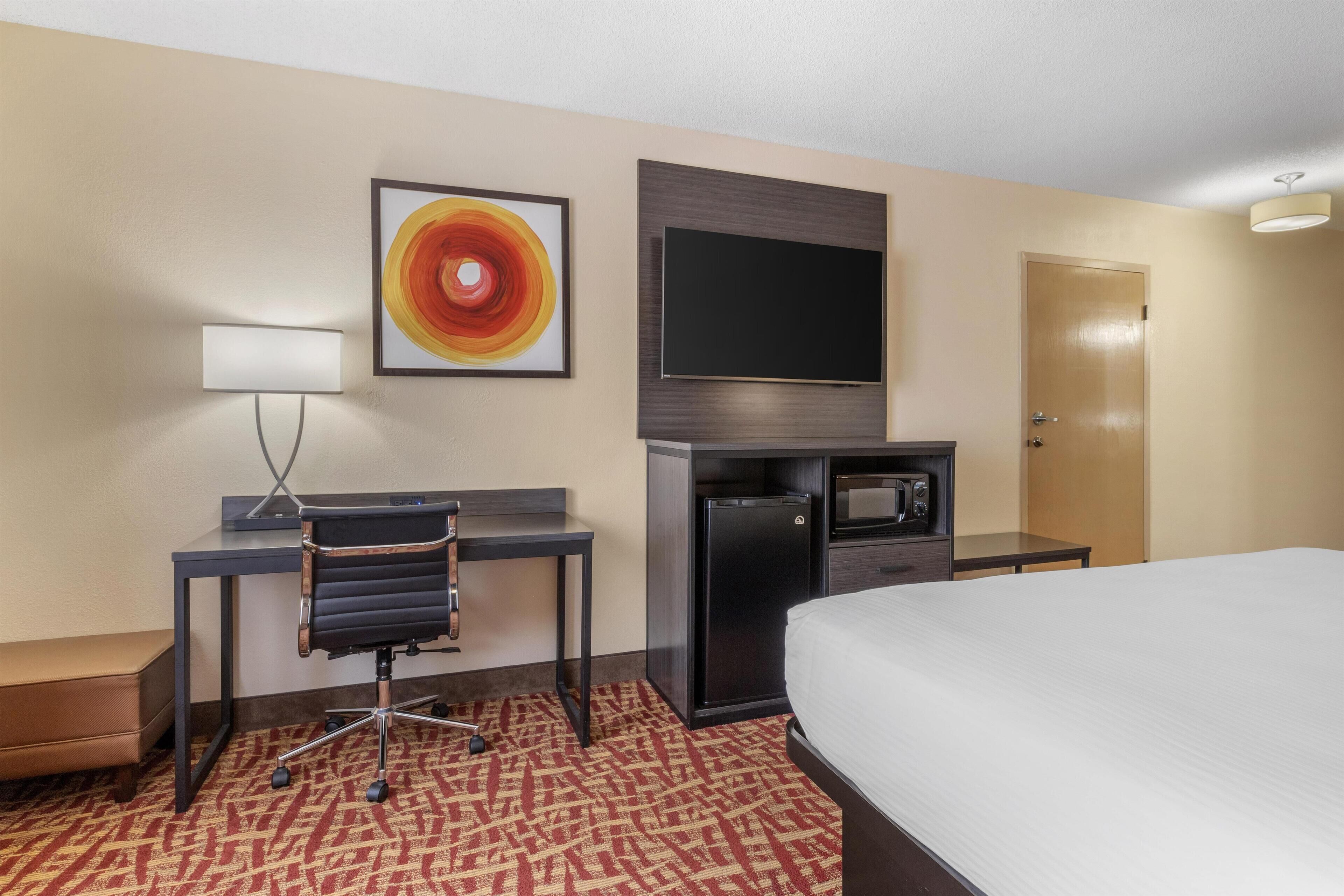 A hotel room with a bed, desk, chair, television, and a microwave.