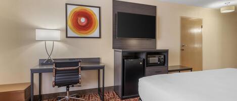 A hotel room with a bed, desk, chair, television, and a microwave.